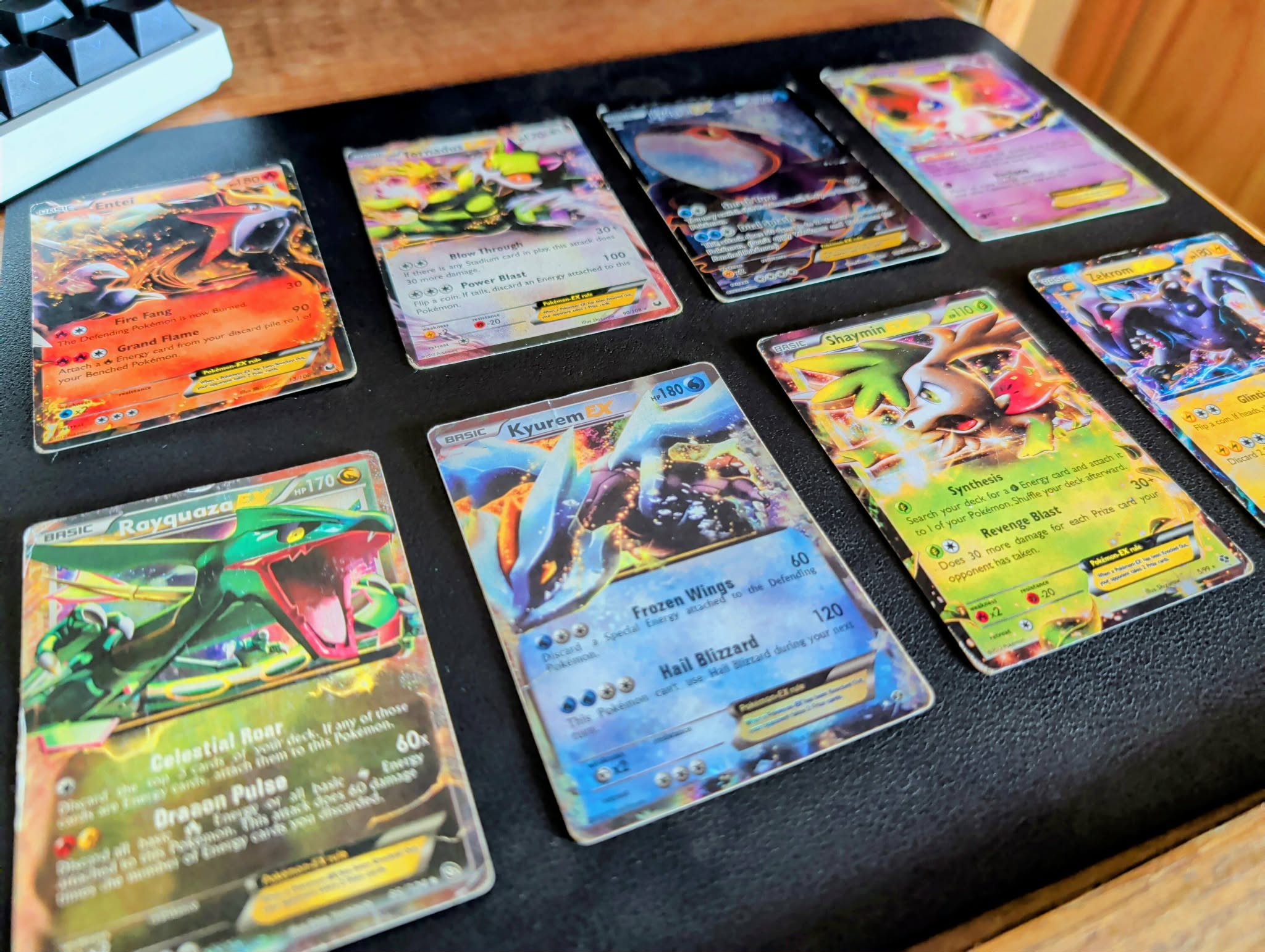 Eight holographic Pokemon EX cards from the XY era laid out on a desk mat, including Entei EX, Rayquaza EX, Kyurem EX and Shaymin EX.